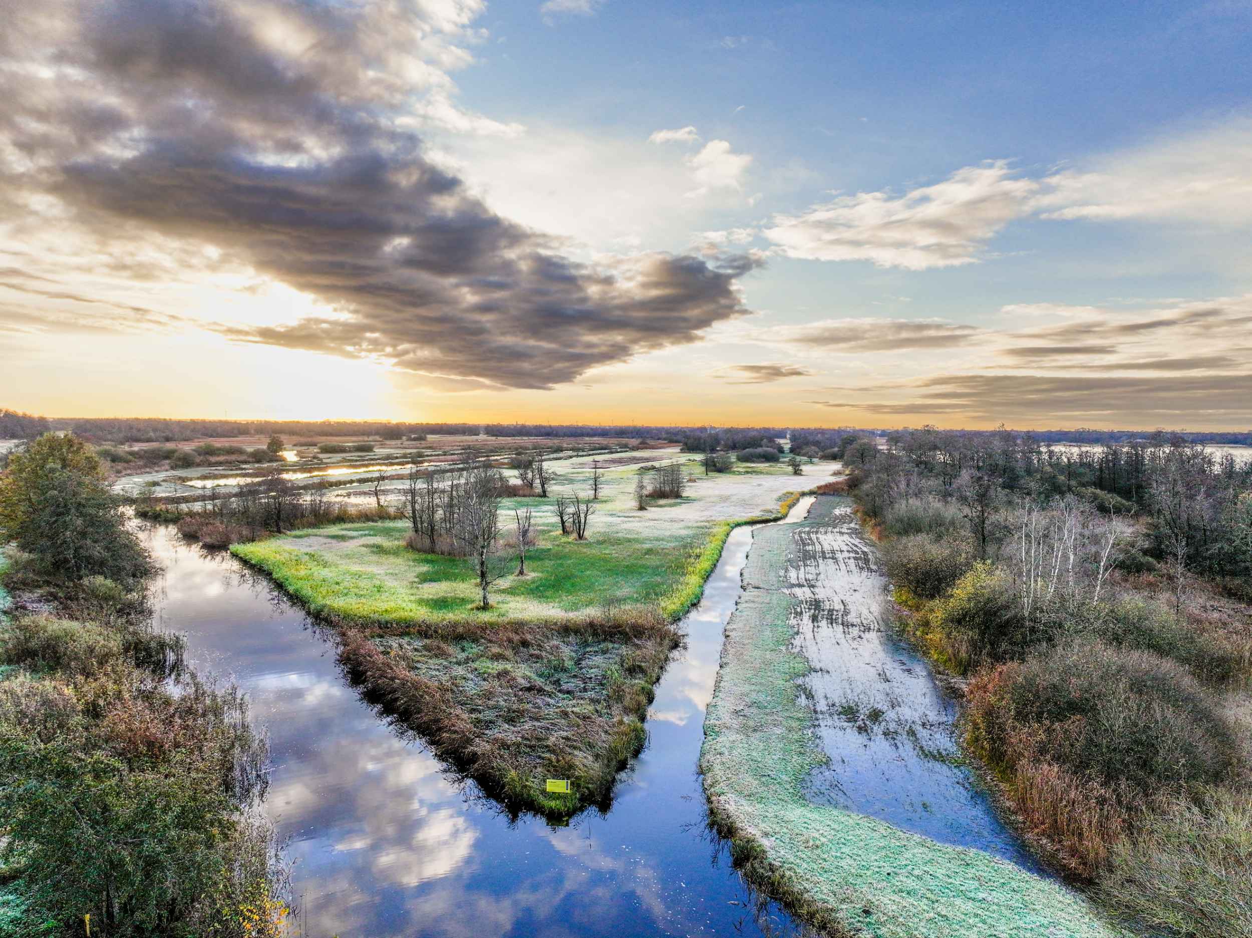 Luchtopname van een natuurgebied met waterlopen en vegetatiestructuren bij zonsopkomst